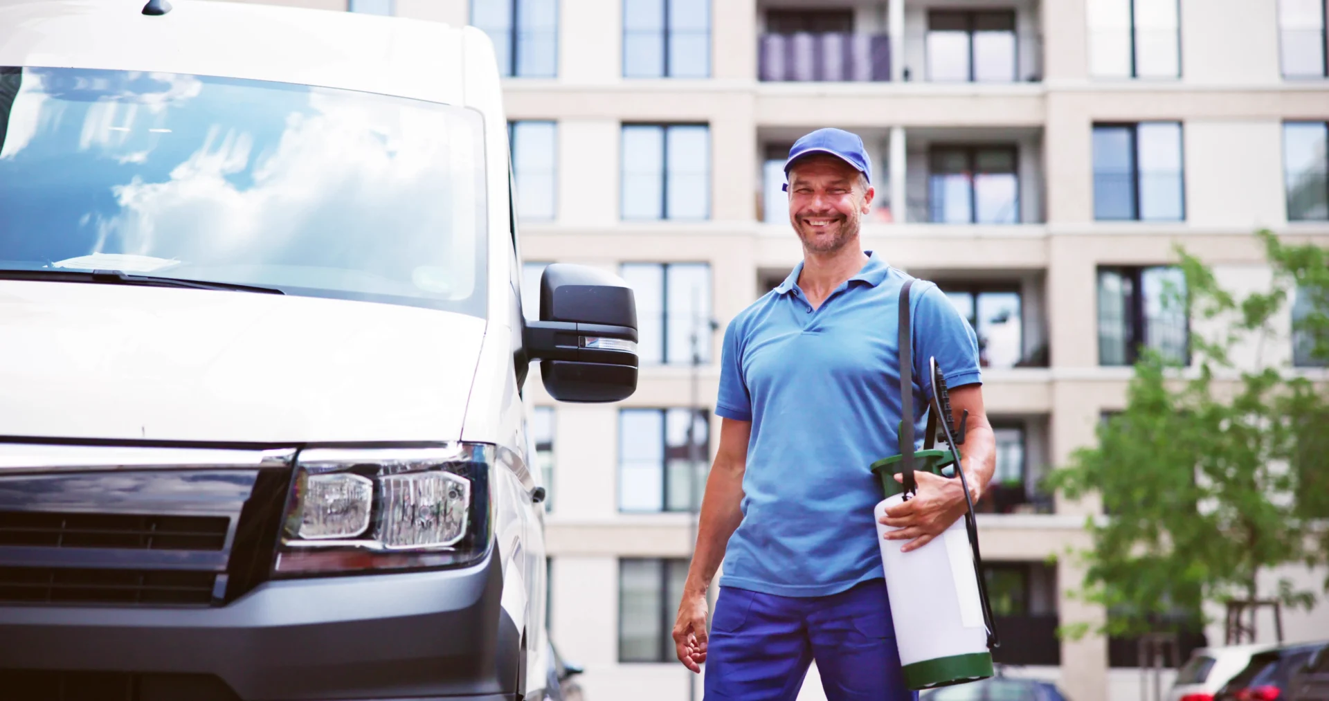 Picture of a smiling Pest Control Technician carrying his tools and standing next to a van.